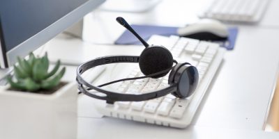 Hotline operator's desk with computer keyboard and modern headset at call centre. Technical support agent's workplace with contemporary equipment. Telemarketing concept